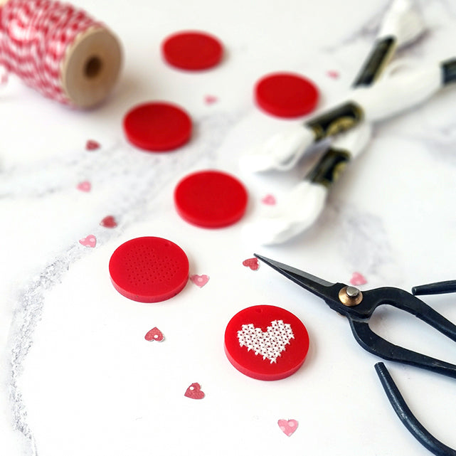 A red heart-shaped button featuring a smaller red heart design in the center.