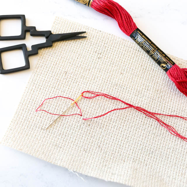 A pair of scissors rests beside a red thread on a wooden table, ready for sewing or crafting tasks.