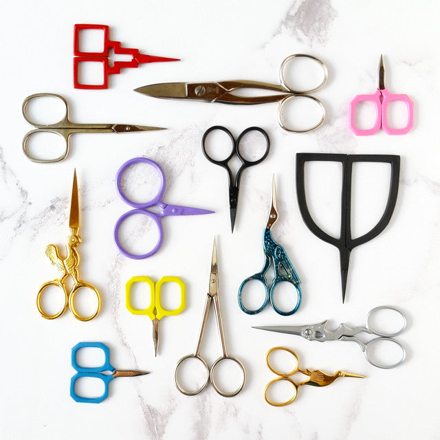 An assortment of colorful embroidery scissors in various shapes and sizes arranged on a marble background.