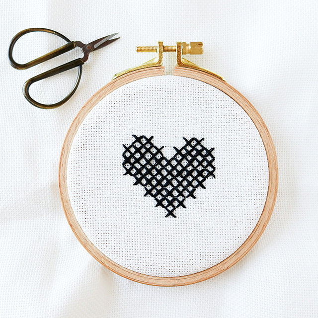 Cross stitch heart design displayed on a wooden embroidery hoop, showcasing intricate stitching and vibrant colors.