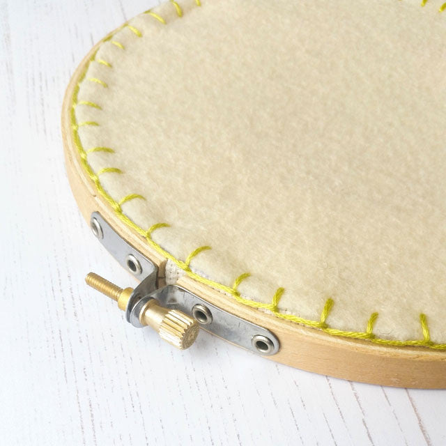 The back of an embroidery hoop finished with a piece of felt, stitched around the edge with bright yellow thread.