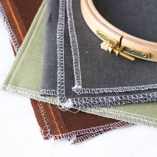 Four fabric pieces in various colors displayed with an embroidery hoop, showcasing intricate stitching designs.