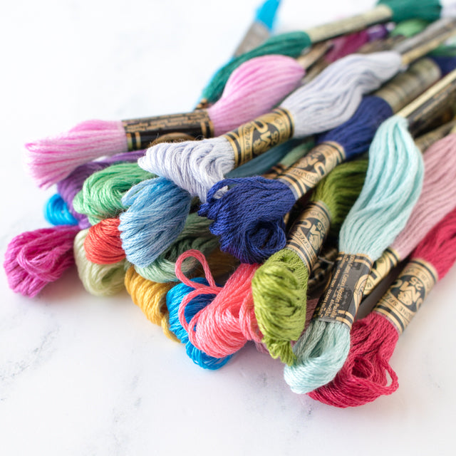 A colorful pile of DMC embroidery floss skeins scattered on a white marble surface.