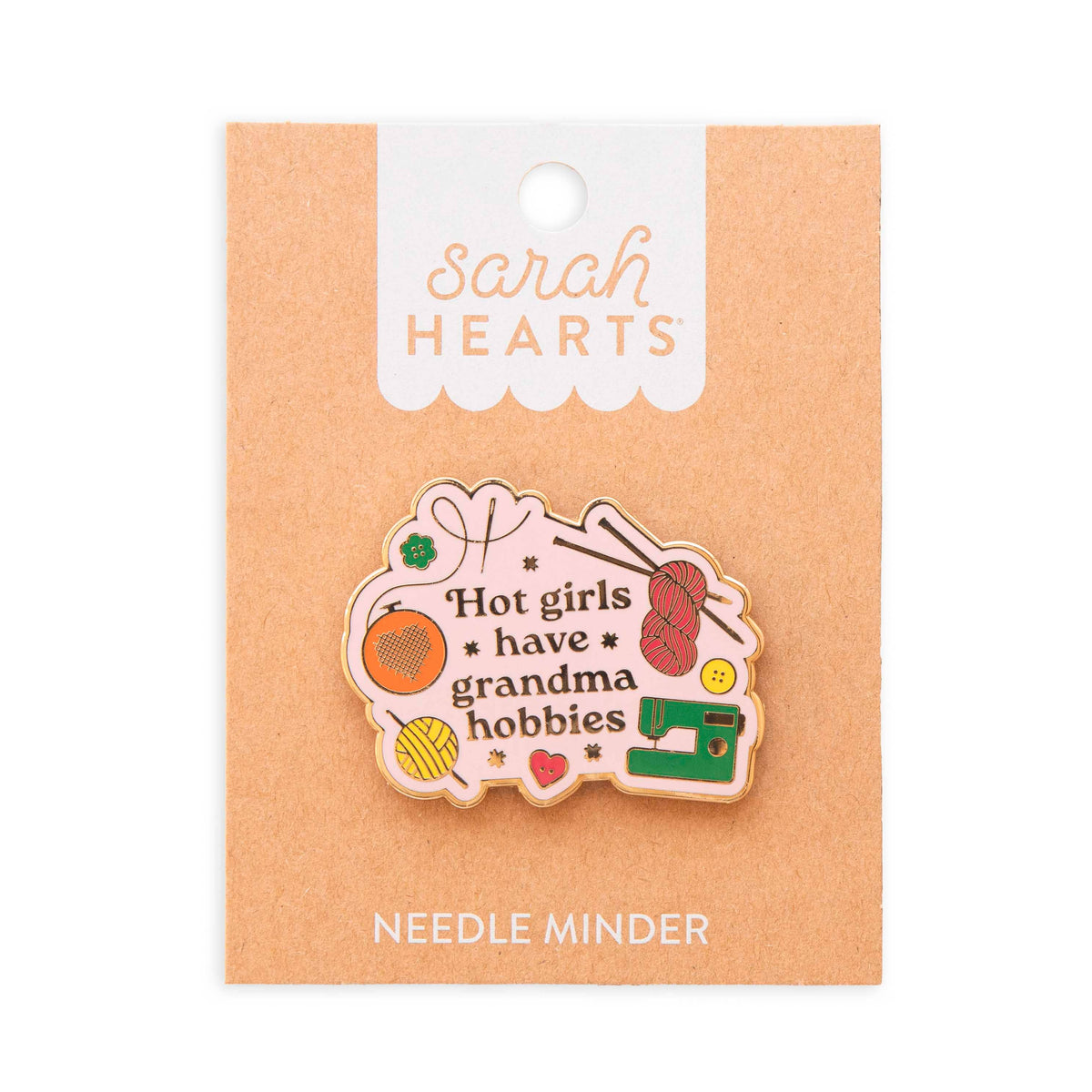 Sarah Hearts needle minder enamel pin reading "Hot girls have grandma hobbies" on a brown cardboard backing.