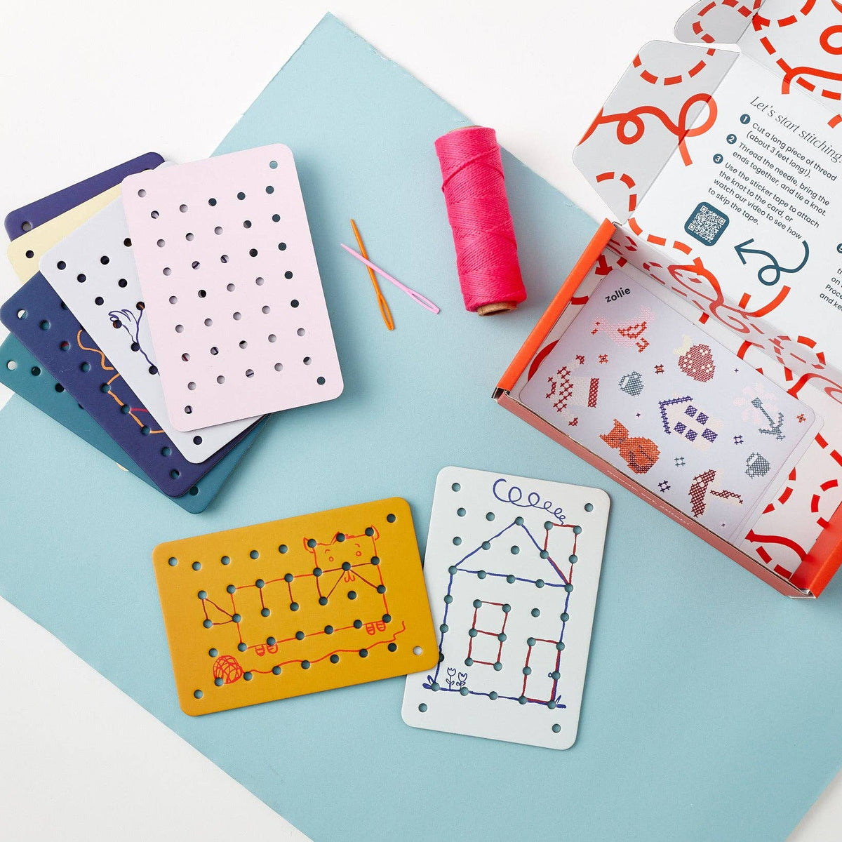 Colorful pegboard cards and thread spool on a light blue mat with an open box containing more cards.