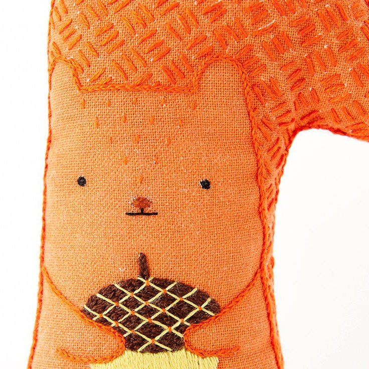 Textile art of a bear holding an acorn on a white background